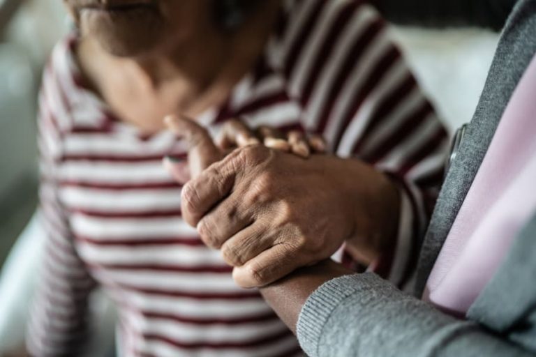Aging adult with Parkinson’s disease holding hands with family member