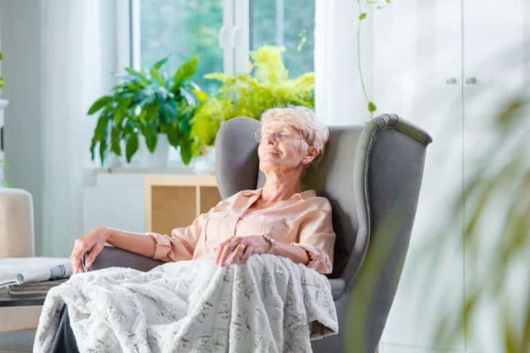 Pleased senior napping in armchair covered with blanket