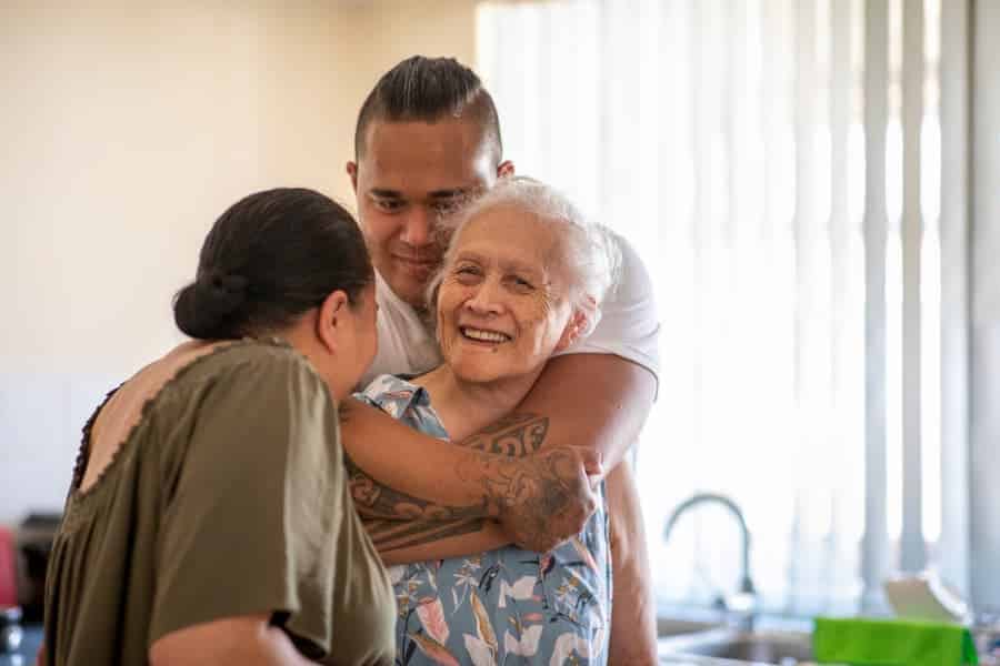 Senior person with relatives cuddling each other in kitchen at home