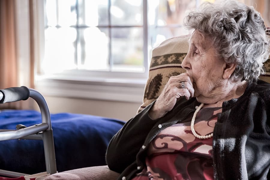 Elderly person sitting in chair in nursing home lost in thought